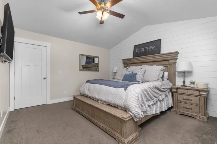 Vaulted ceiling featuring a ceiling fan, white paneled accent wall, and neutral wall paint