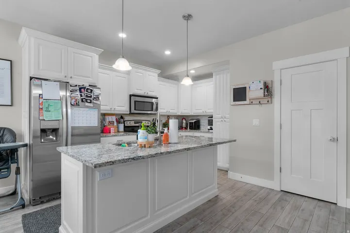 Kitchen featuring white cabinetry, stainless steel appliances, a granite-finish island, two pendant lights, and wood-finish flooring