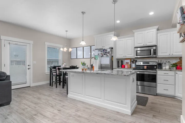 White cabinetry, stainless steel appliances, granite countertops, wood-finish flooring, and recessed lighting