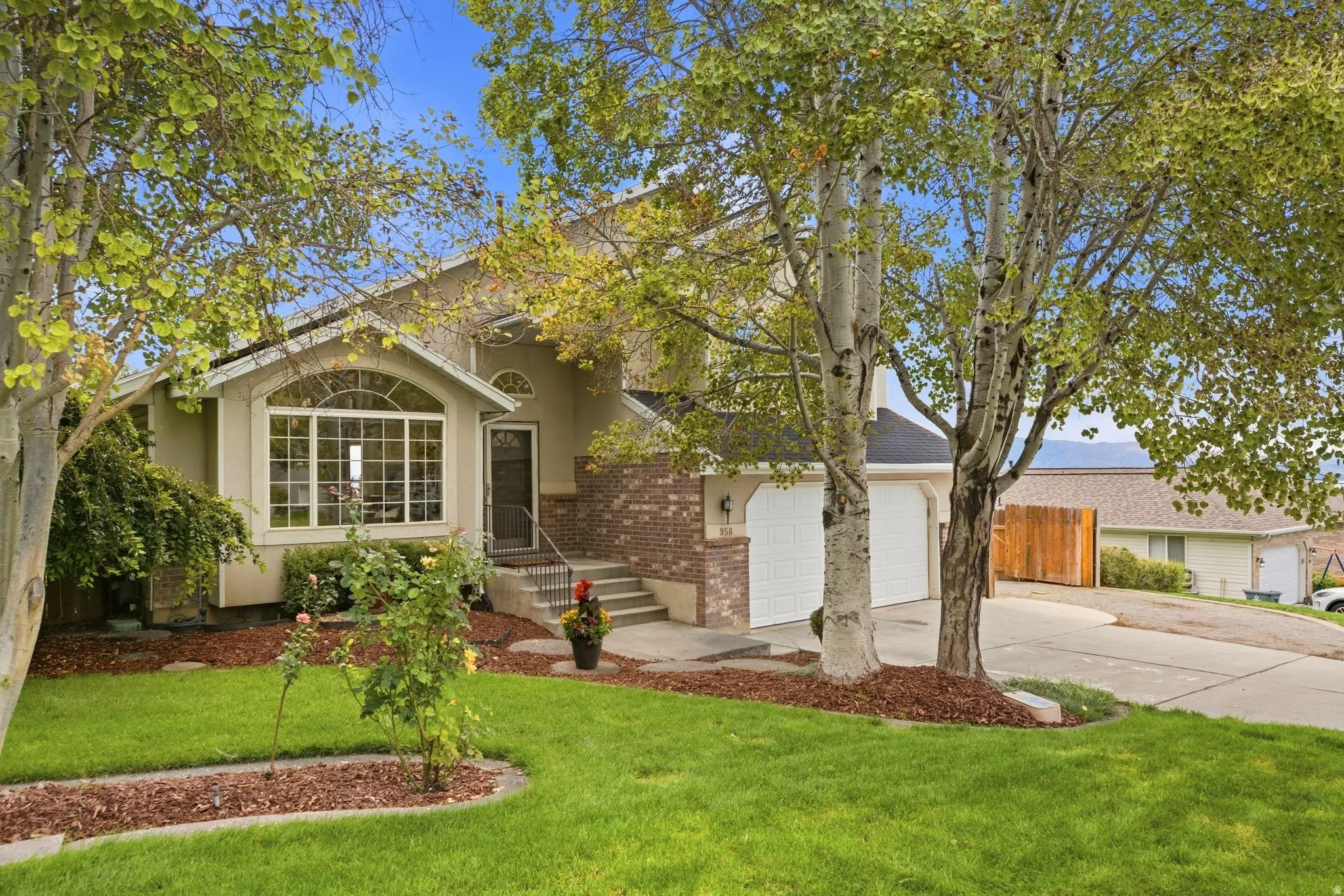 Front view of the home with mature landscaping, large windows, and a two-car garage