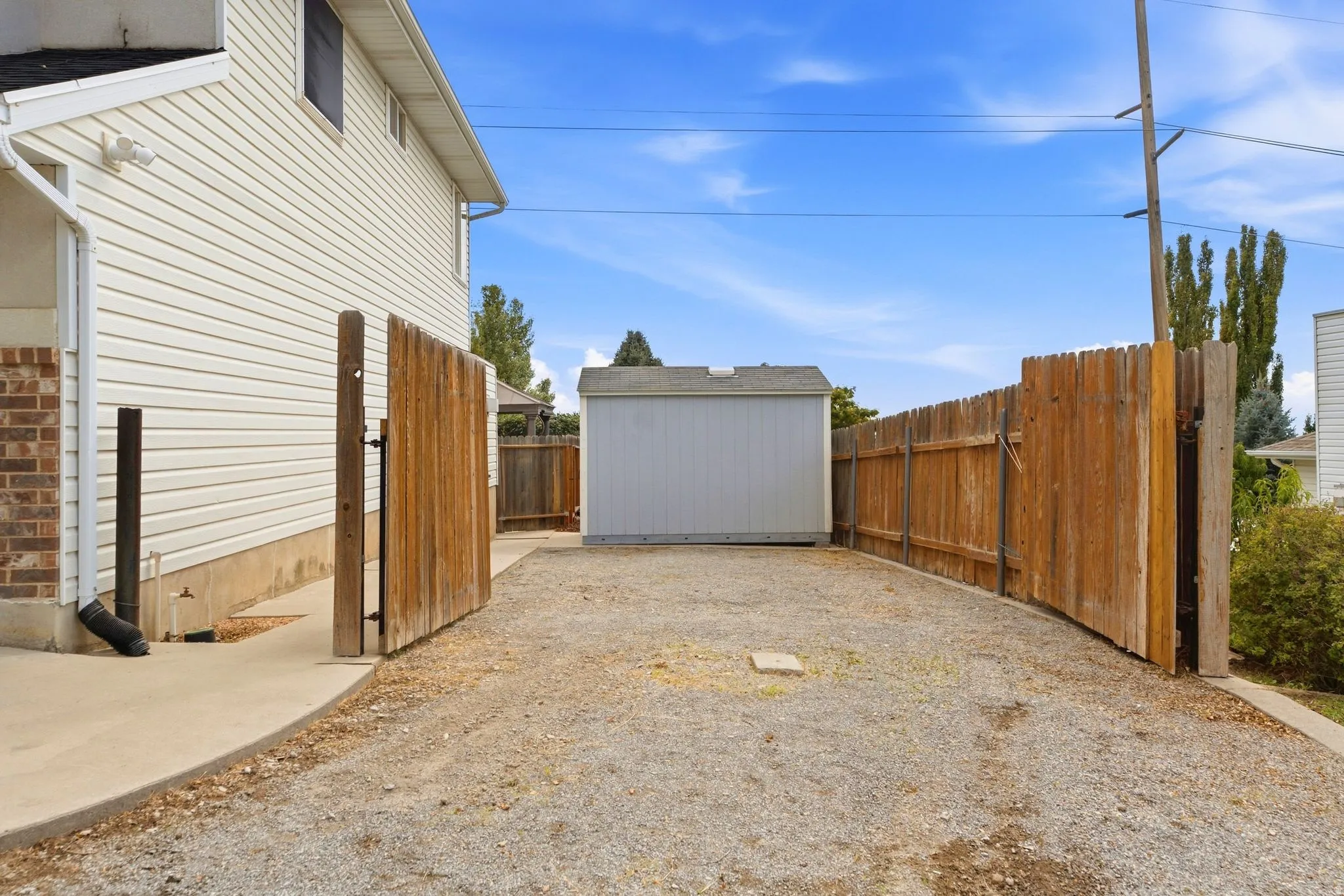 View of the double-wide opened gate, detached shed, and storage for toys, RV, boat, or camper.