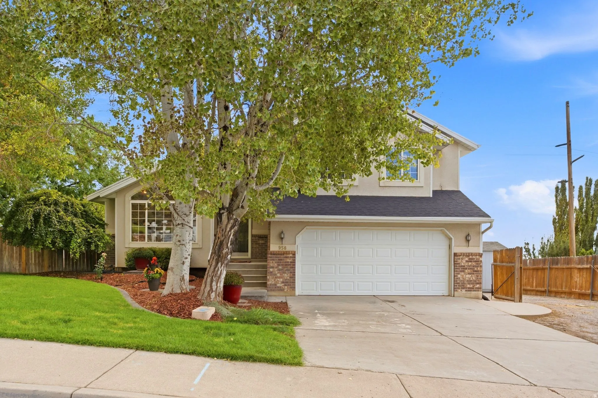 Front view of the home with mature landscaping, large windows, and a two-car garage