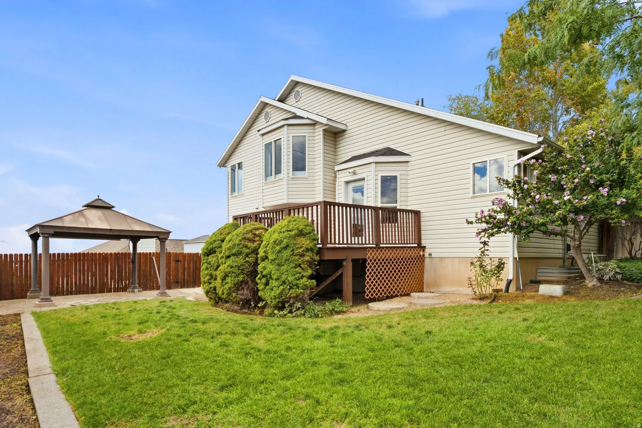 Expansive backyard featuring a wood privacy fence, a detached gazebo, and mature landscaping