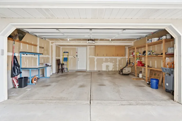 Attached 2-car garage with rear access door into the living room, room for storage, and built-in shelving