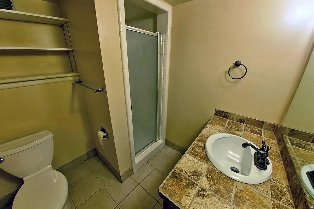Walk-in shower with clear glass enclosure, tiled vanity countertop, integrated sink, and built-in shelving