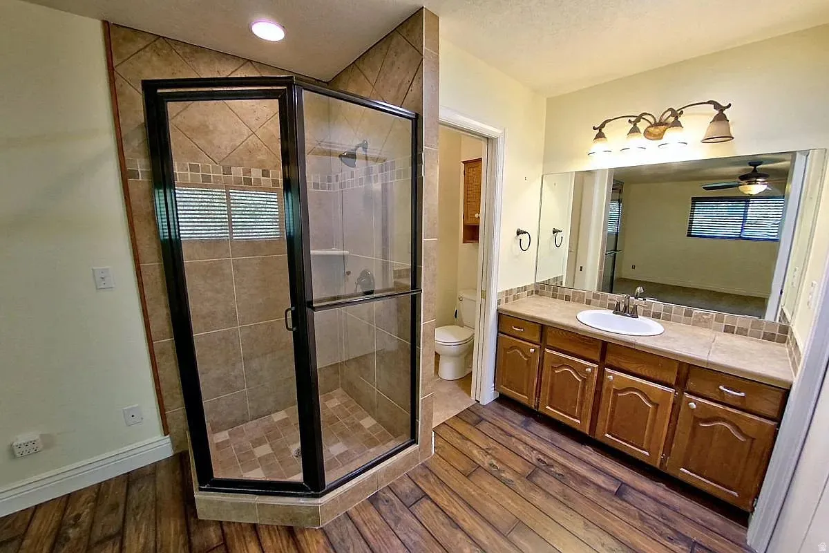 Spacious bathroom featuring a glass-enclosed shower with tile surround, a single vanity with a large mirror, and wood-finish flooring
