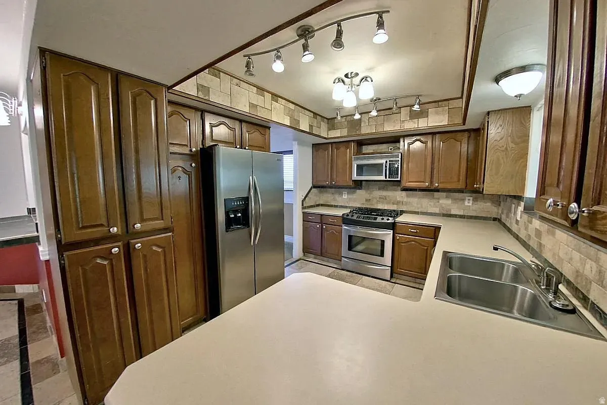 Warm wood cabinetry, stainless steel appliances, dual basin sink, and track lighting