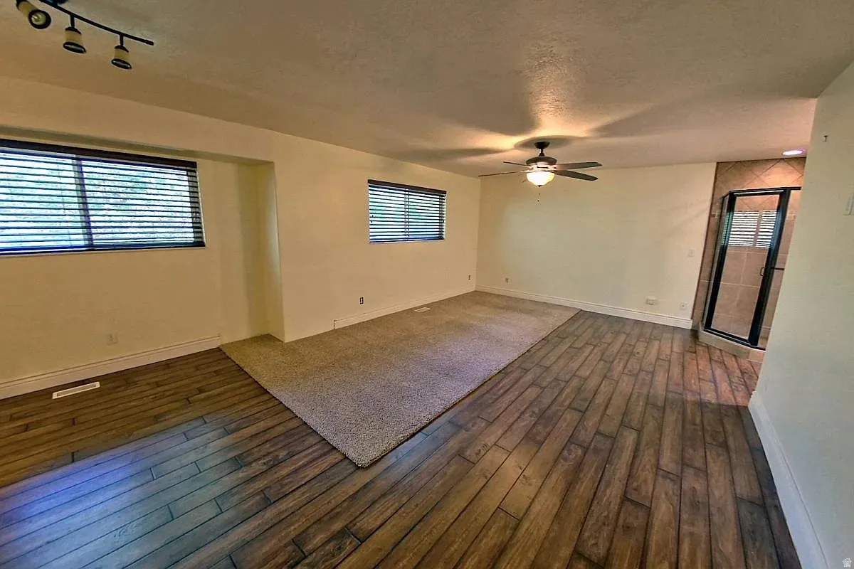 Wood-finish flooring, recessed lighting, ceiling fan, carpeted area, and a tiled shower enclosure with a glass door
