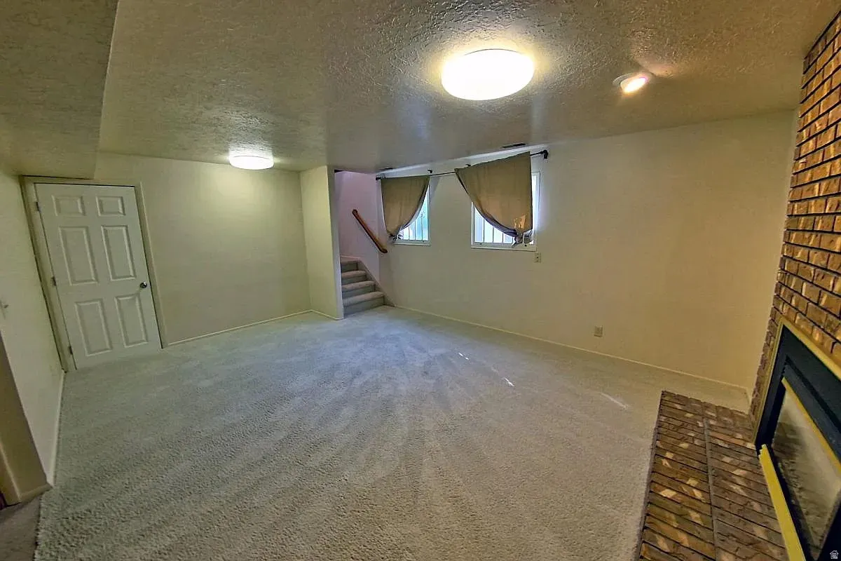 Carpeted living space featuring a brick-clad fireplace, two windows, and a staircase