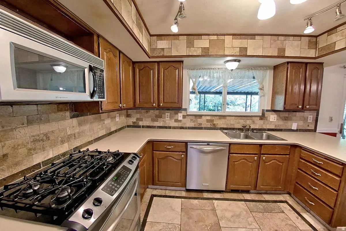 Kitchen featuring wood cabinetry, stainless steel gas range, over-the-range microwave, double basin sink, and tile flooring with border detail