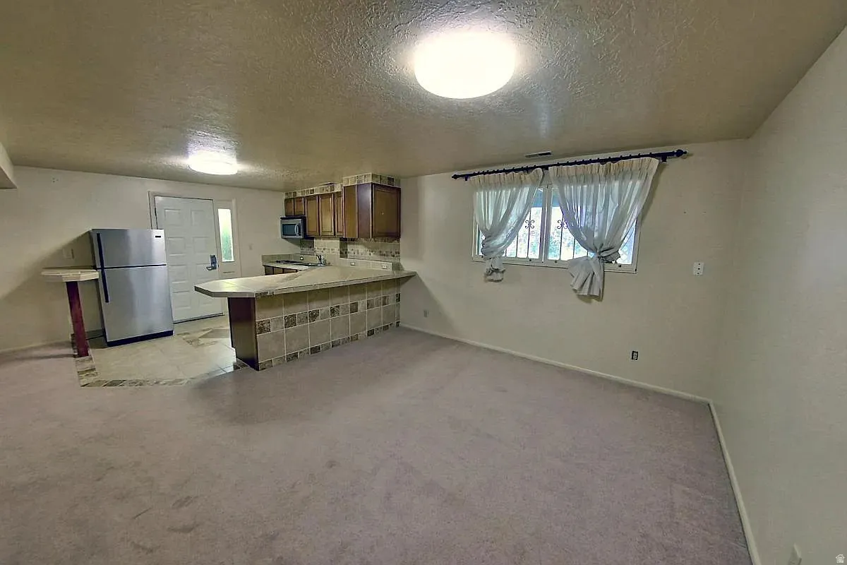 Kitchenette with wood cabinetry and tile backsplash, stainless steel refrigerator, and a breakfast bar with stone-finish countertop