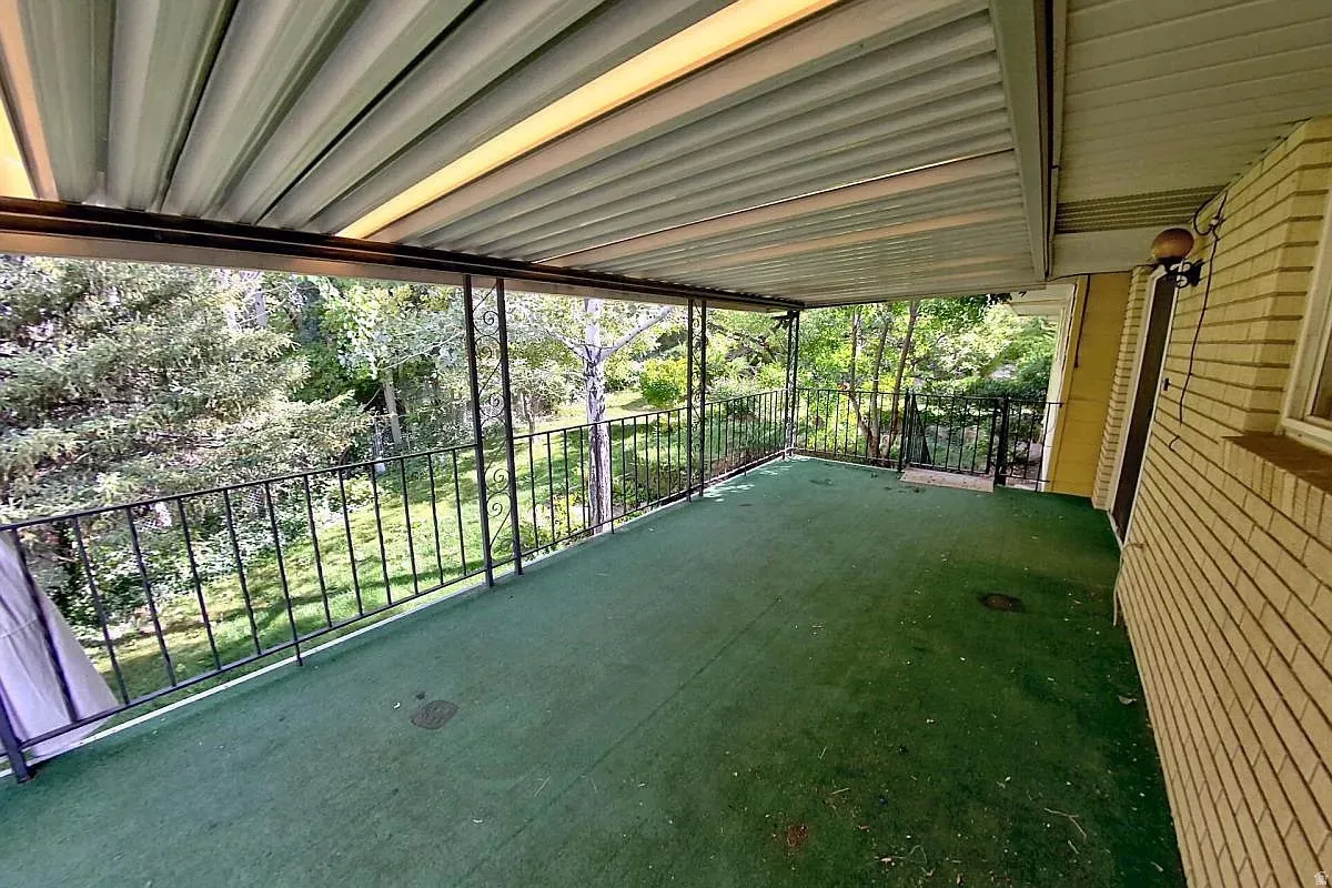 Covered patio featuring a green outdoor carpet, black metal railing, and a brick exterior wall