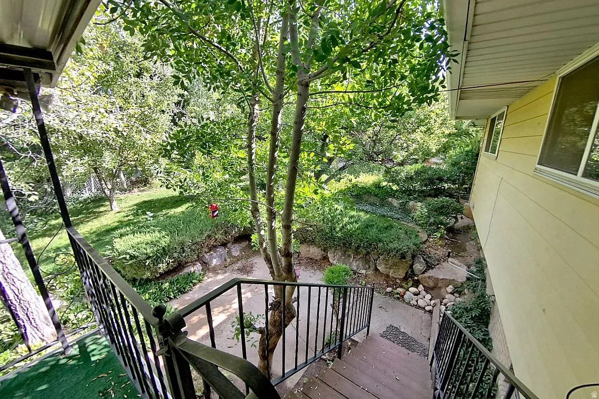Exterior stairs with black wrought iron railing, leading to a landscaped yard with mature trees and established plantings