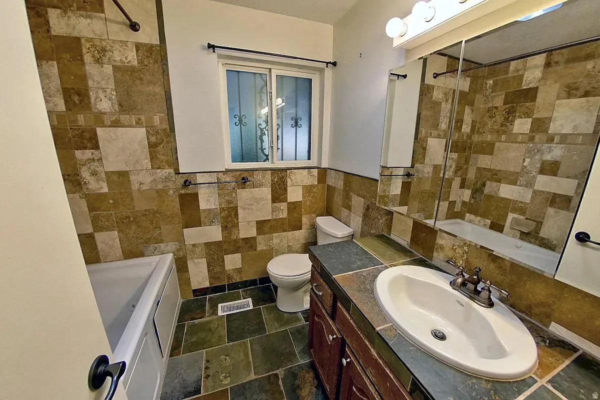 Tiled bathroom featuring a built-in bathtub, a window with decorative ironwork, a toilet, a vanity with a drop-in sink, and a built-in medicine cabinet
