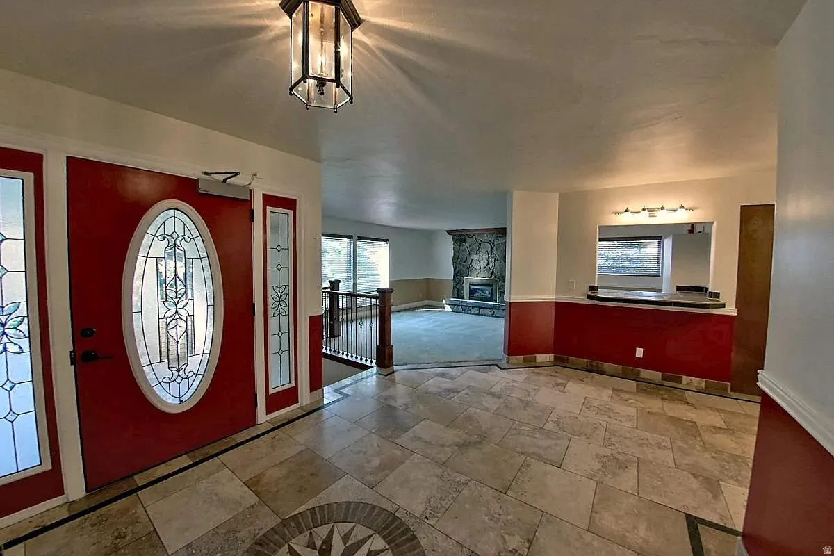Entry featuring a red door with decorative glass, coordinating side lights, a hexagonal ceiling fixture, and a tiled floor with an inlaid medallion