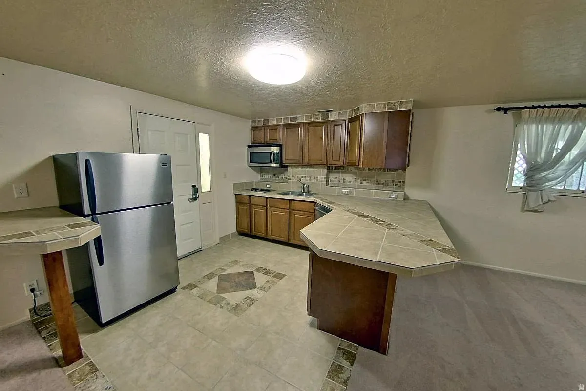 Full kitchen with tile countertops, wood cabinetry, stainless steel appliances, and a tile backsplash