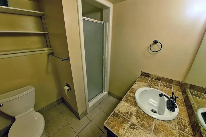 Walk-in shower with clear glass enclosure, tiled vanity countertop, integrated sink, and built-in shelving