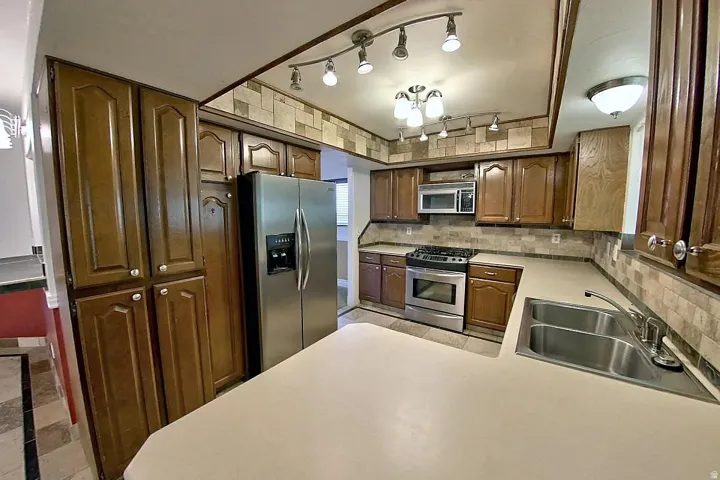 Warm wood cabinetry, stainless steel appliances, dual basin sink, and track lighting