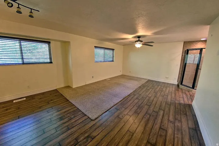 Wood-finish flooring, recessed lighting, ceiling fan, carpeted area, and a tiled shower enclosure with a glass door