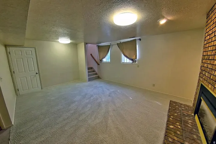 Carpeted living space featuring a brick-clad fireplace, two windows, and a staircase