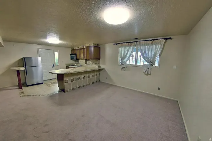 Kitchenette with wood cabinetry and tile backsplash, stainless steel refrigerator, and a breakfast bar with stone-finish countertop