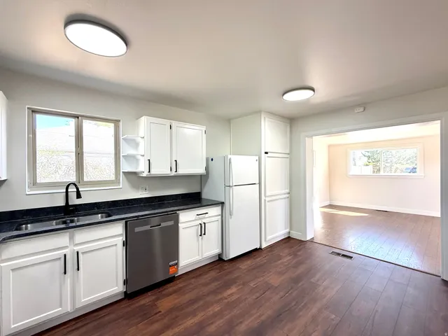 Kitchen featuring white cabinetry, dark countertops, wood-finish flooring, and stainless steel dishwasher