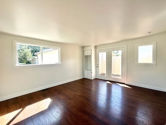 Wood-finish flooring, white walls, built-in cabinetry, dual French doors, and multiple windows