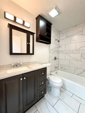 Dark wood-finish vanity with a light speckled countertop, white undermount sink, and chrome faucet