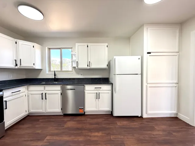 Kitchen with dark wood-finish flooring, white cabinetry, dark countertops, and a stainless steel dishwasher