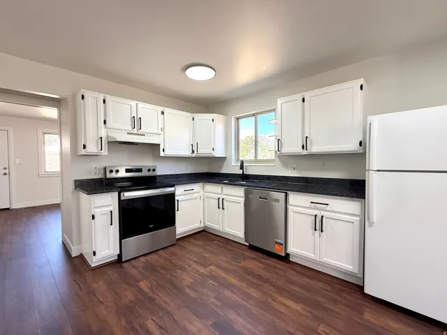 Kitchen featuring white cabinetry, dark countertops, wood-finish flooring, and stainless steel appliances