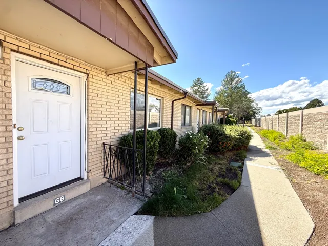 Brick exterior with a covered entry, decorative glass door, established landscaping, and an adjacent walkway