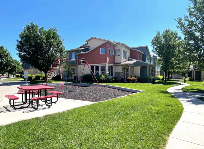 Expansive green lawn, a winding concrete pathway, mature trees providing shade, and a playground area with a swing set