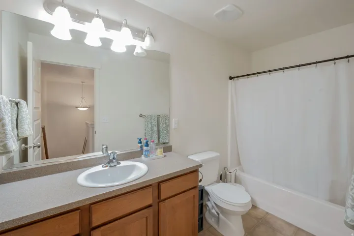 Bathroom featuring a large vanity mirror, wood-finish cabinetry, a single basin sink, a bathtub with an integrated shower, and tiled flooring