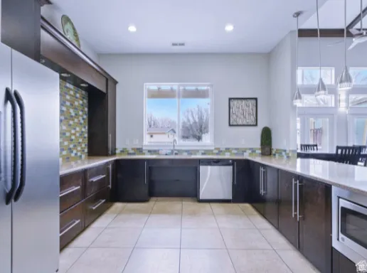 Spacious kitchen featuring dark wood-finish cabinetry, tile flooring, stainless steel appliances, and a mosaic tile backsplash