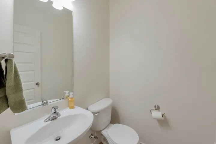 Pedestal sink with chrome faucet, wall-mounted mirror, and white toilet