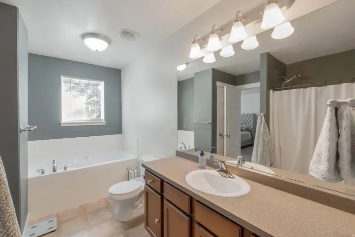 Built-in bathtub, vanity with integrated sink, extended countertop, wood-finish cabinetry, and tiled flooring