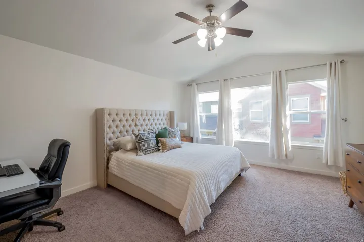 Vaulted ceiling, carpeted flooring, white walls, ceiling fan, and multiple windows