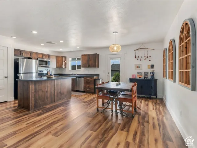 Open-concept kitchen with wood-finish flooring, dark wood cabinetry, a central island, and stainless steel appliances