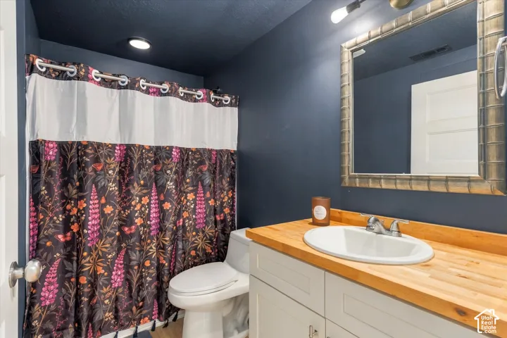 Built-in vanity with wood-finish countertop, undermount sink, and wall-mounted mirror