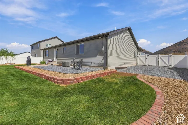 Backyard featuring a manicured lawn, gravel patio, brick-edged landscaping, and white privacy fencing