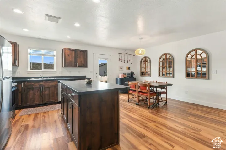 Kitchen and dining area featuring wood-finish flooring, dark wood cabinetry, a central island, and recessed lighting