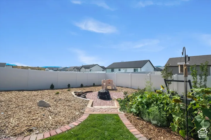 Expansive backyard featuring a brick paver pathway, a dedicated fire pit area, and a white privacy fence