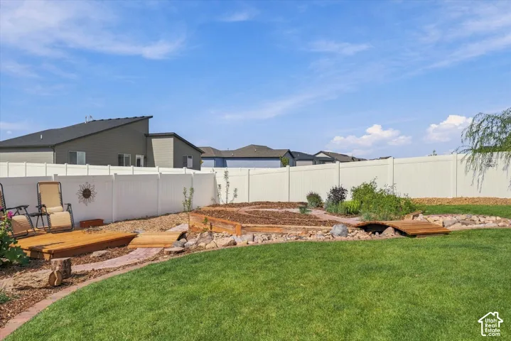 Expansive backyard featuring a manicured lawn, white privacy fencing, and a decorative garden area with a wooden bridge