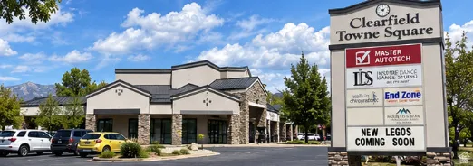 Clearfield Towne Square commercial building featuring a stone and stucco exterior, dark roof, expansive parking lot, and prominent signage