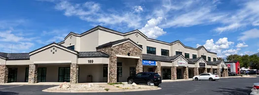 Commercial building featuring a stone and stucco exterior, multiple storefronts with large glass entrances, and a dark shingle roof