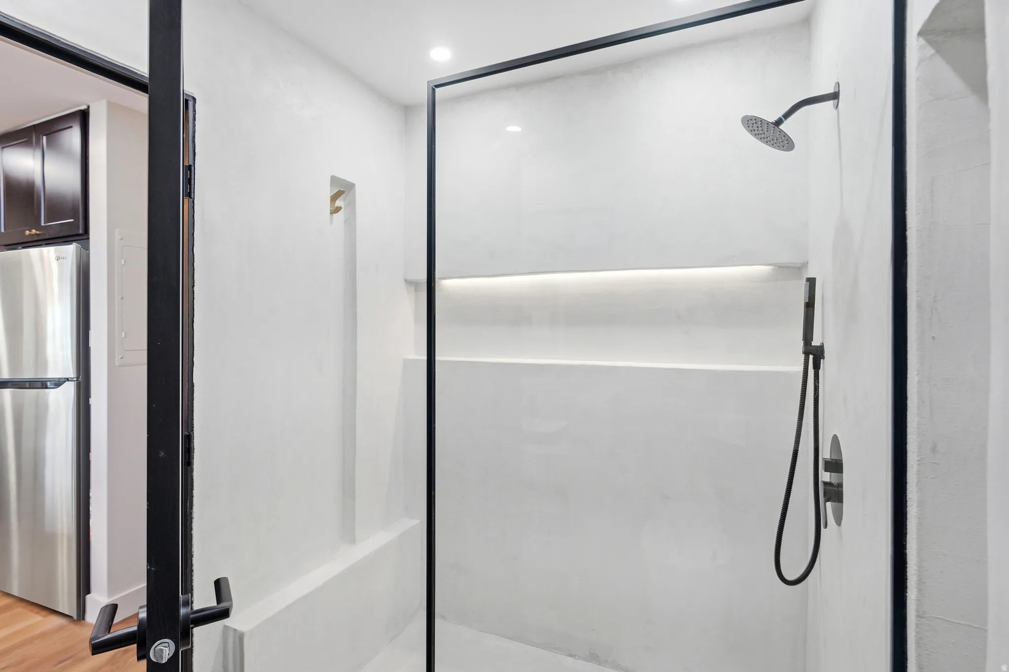 Enclosed shower with a frameless glass panel, integrated niche shelving, matte black fixtures, and a recessed ceiling light
