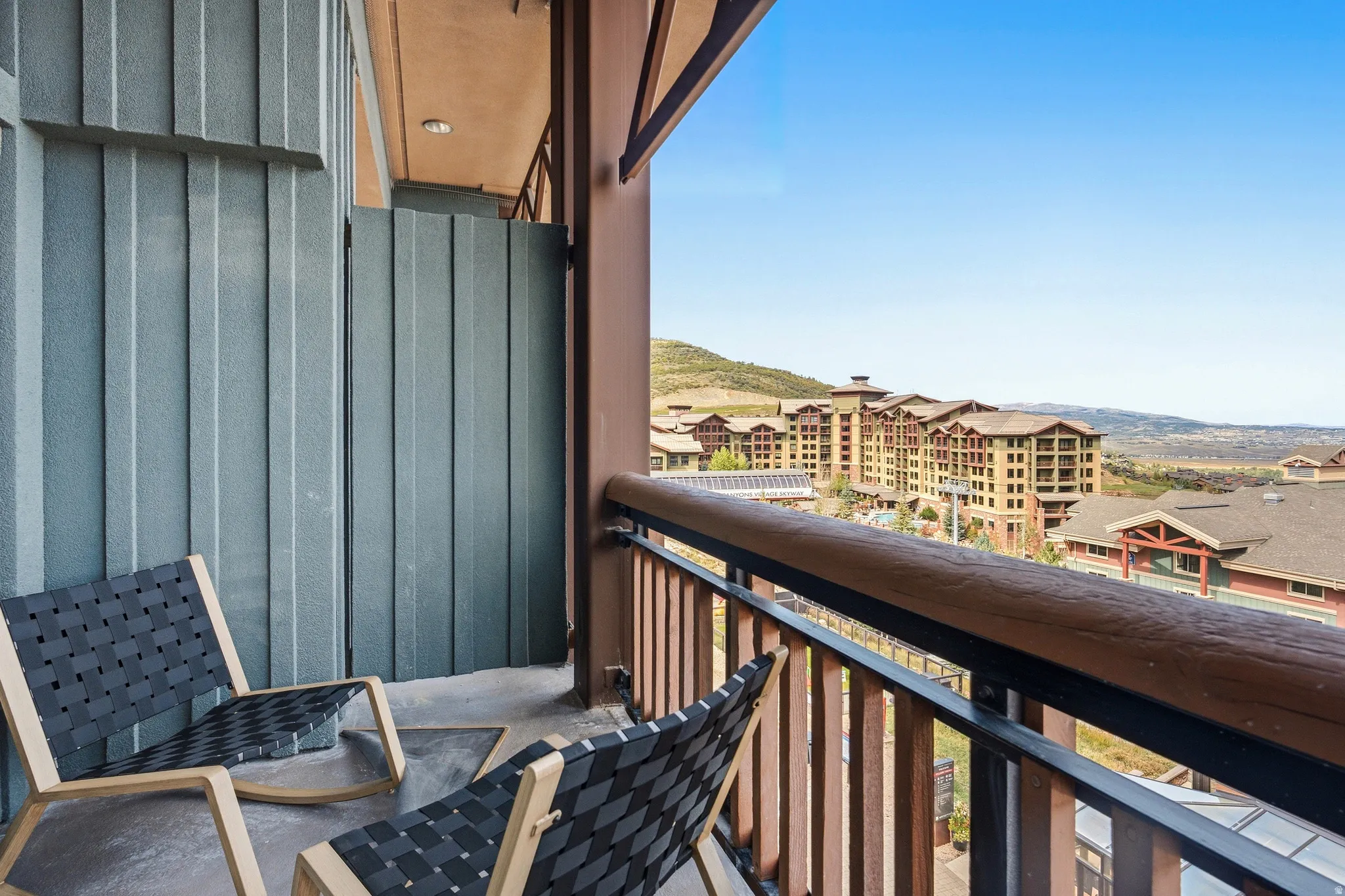 Balcony with a textured concrete floor, a privacy wall, and iron railings with a wood-finish top rail