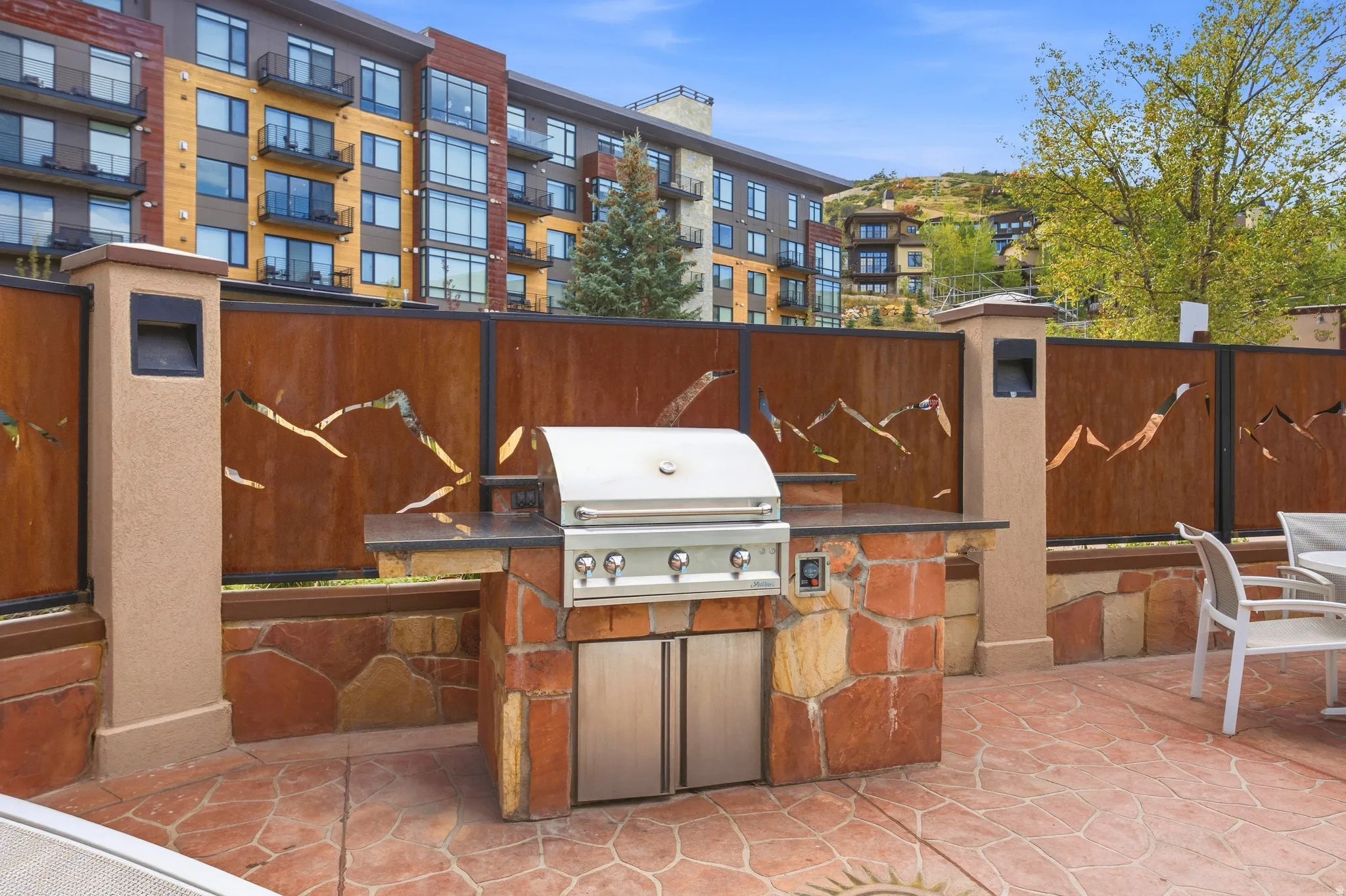 Outdoor kitchen with built-in stainless steel grill, stone base, and dark countertop