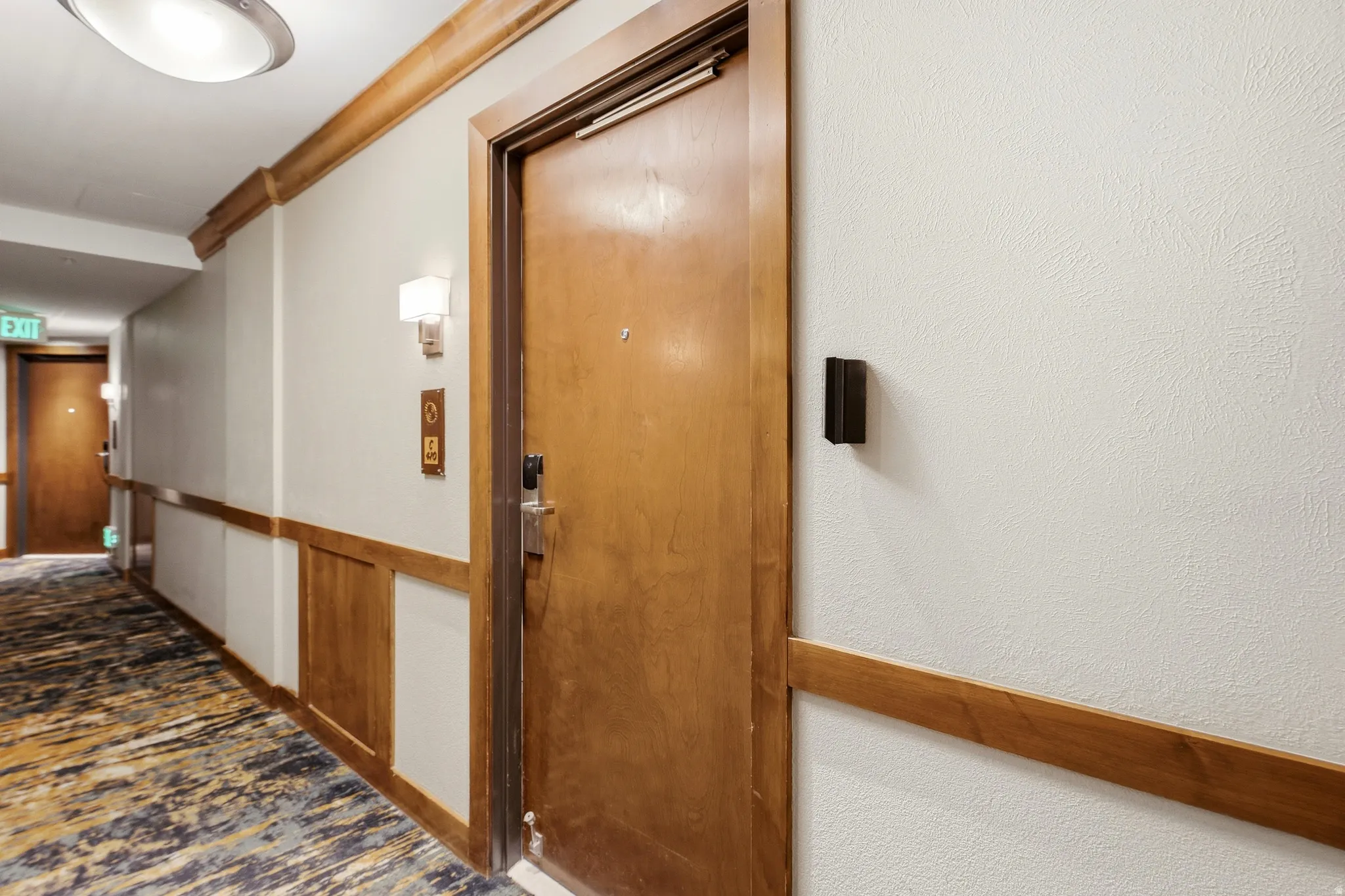 Corridor featuring wood-panel wainscoting, textured walls, and a patterned carpet