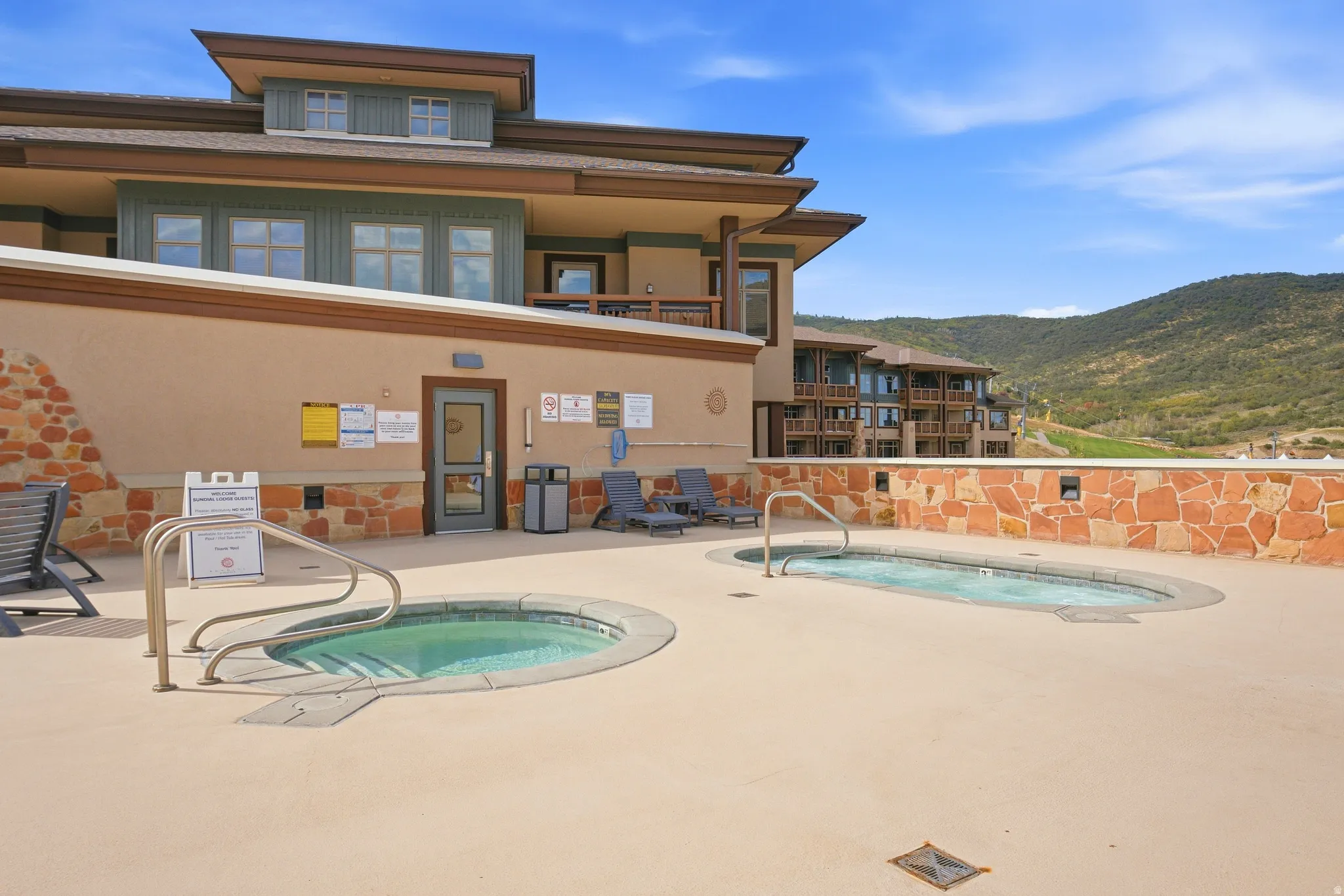 Two outdoor spas on a neutral-toned hardscape with mountain scenery
